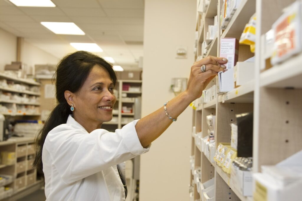 Farmacêutica de jaleco branco organizando produtos nas prateleiras da farmácia